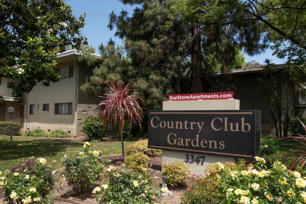Sign and beautiful landscaping next to apartment building at Country Club Gardens in Sacramento, California